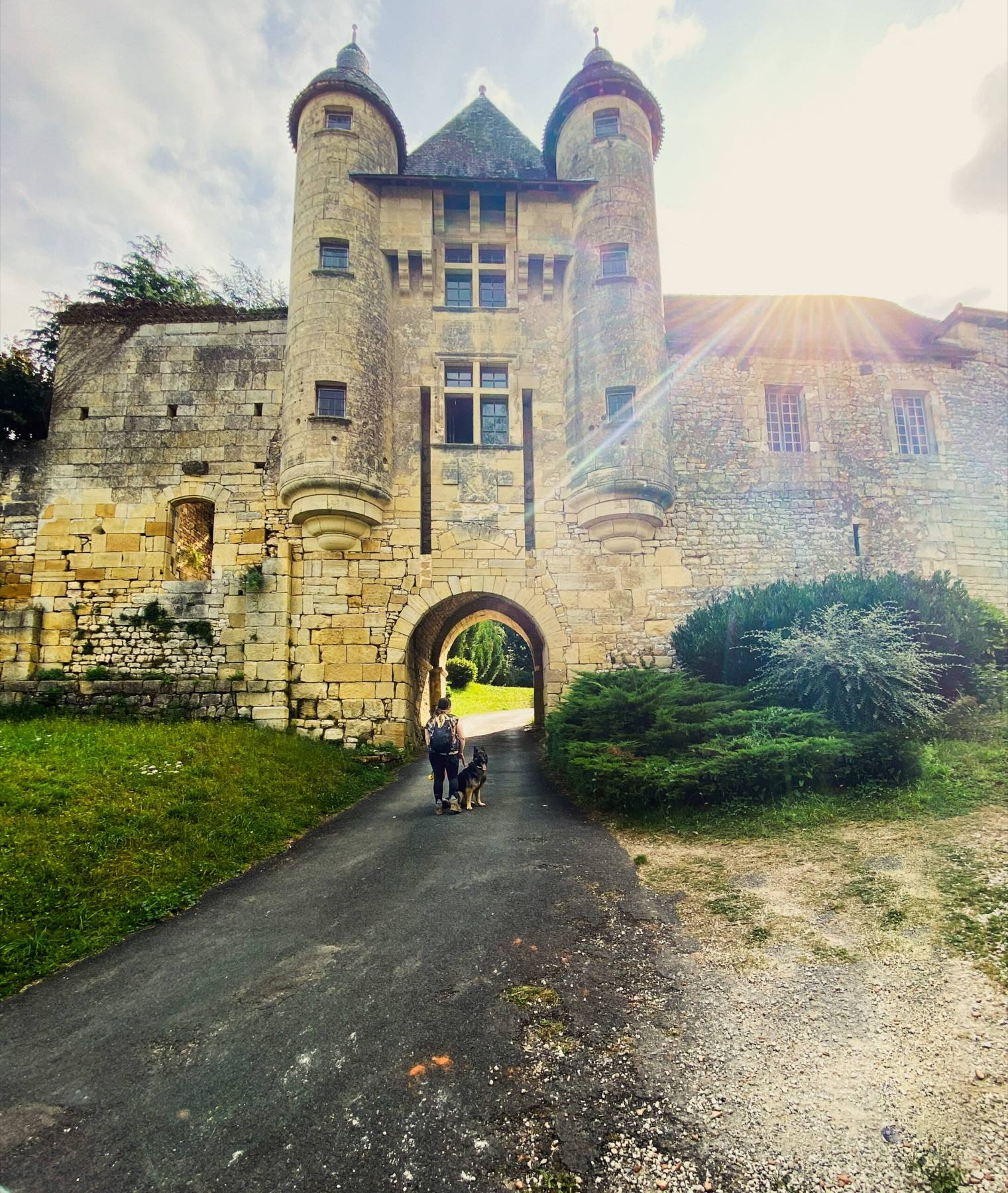 Melissa and Arya walking towards the gateway of a sunlit stone château with round towers