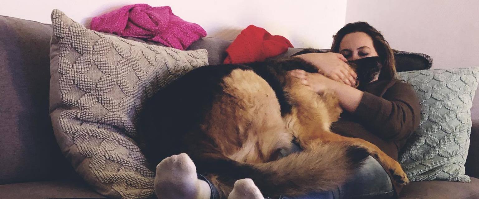 Melissa curled up on a sofa with her arms around Rex, a big black-and-tan dog