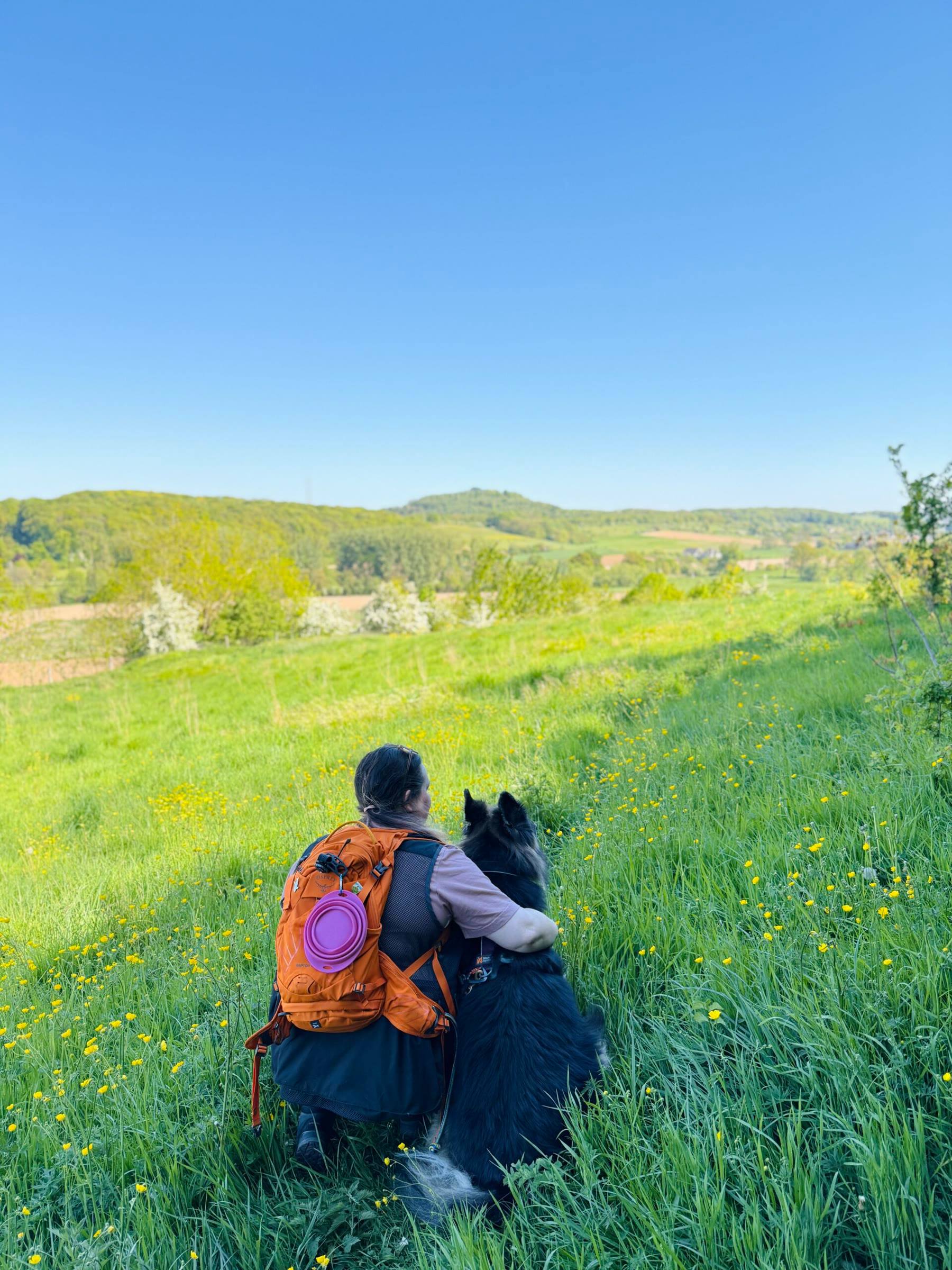 Melissa with her orange backpack and Arya, overlooking the rolling hills of South Limburg