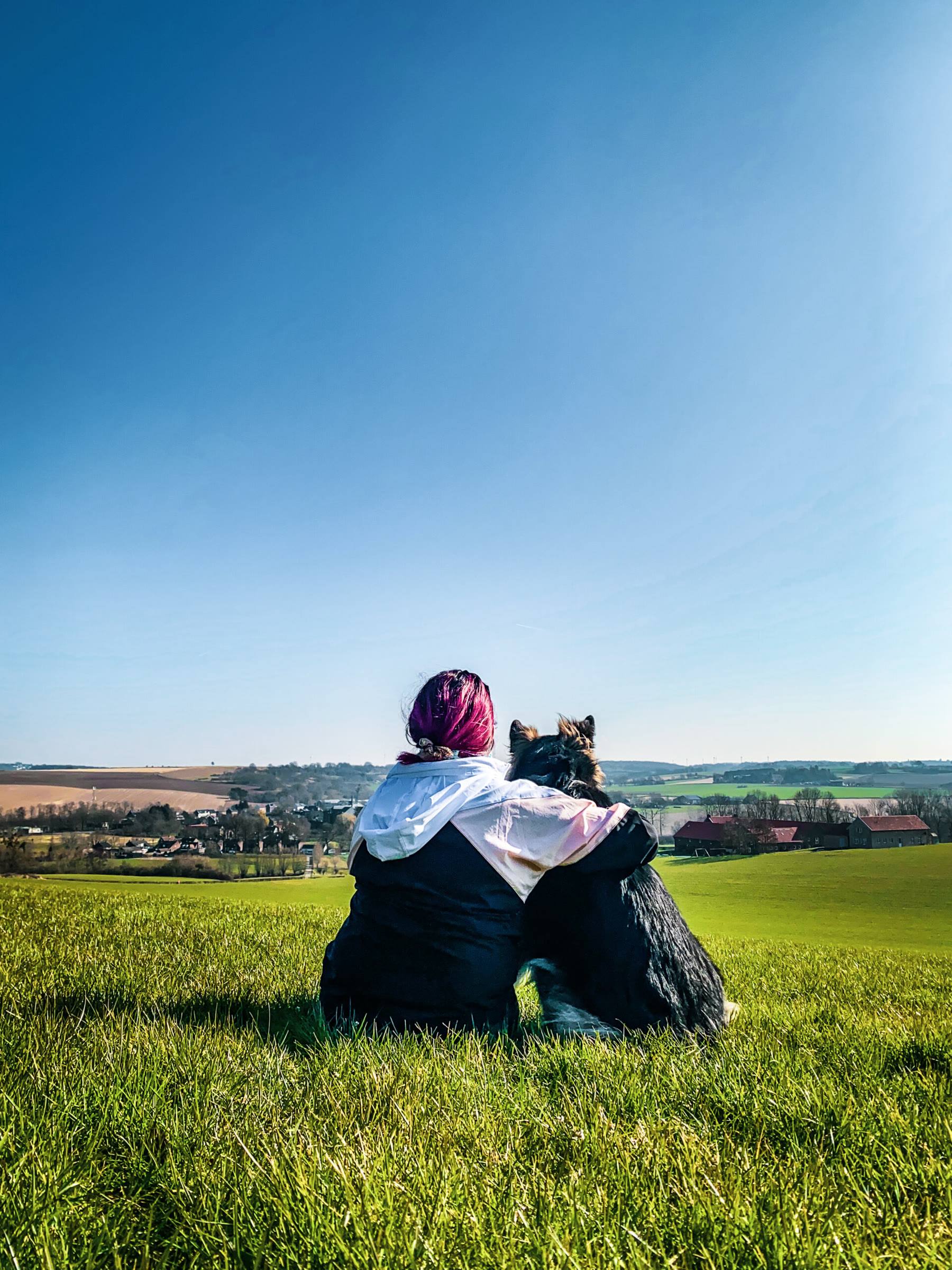 Melissa and Arya sitting side by side on a green hilltop, looking out over the valley