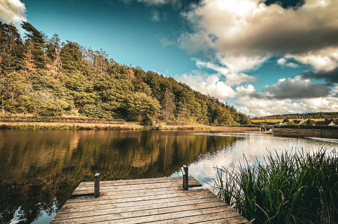 A wooden jetty on a calm lake surrounded by green hills