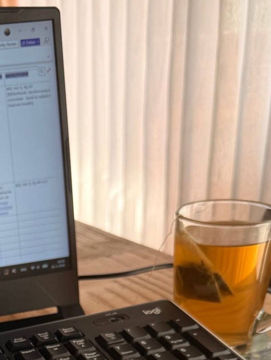 A study desk with an open laptop, a keyboard and a glass of tea in soft daylight
